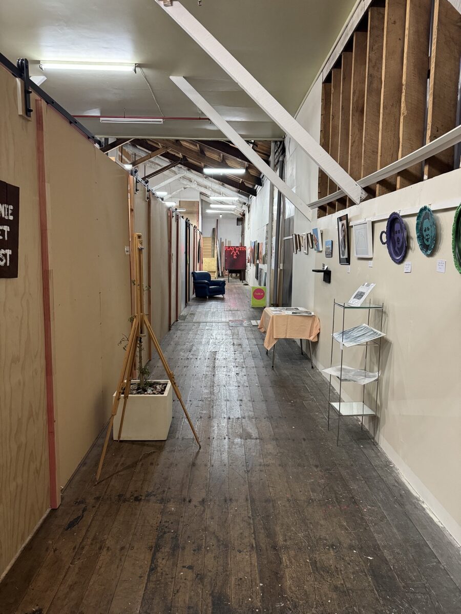 Long timber-floored corridor lined with artist studios, an easel and artwork on the walls