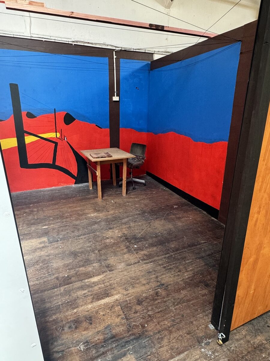 Empty artist studio with a hand-painted red and blue mural, a small table and a chair